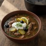 Тарелка сборной мясной солянки со сметаной, кружком лимона, маслинами и зеленью
