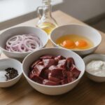 Куриная печень, лук, яйцо, сметана, мука и специи на кухонном столе