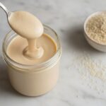 Банка кунжутной пасты тахини, ложка и рассыпанный кунжут